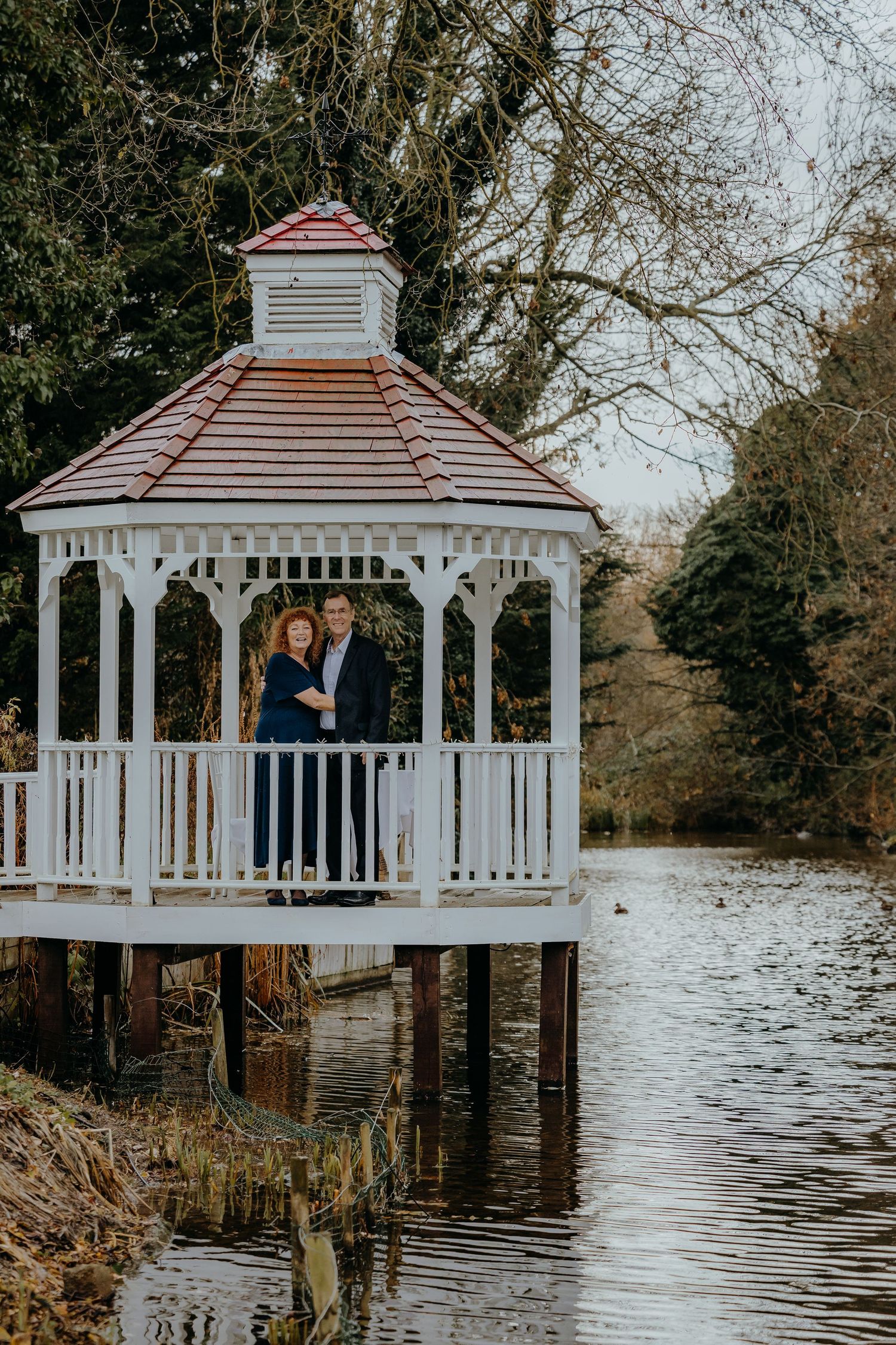 A white gazebo stands over water with a couple visible inside during an overcast day.