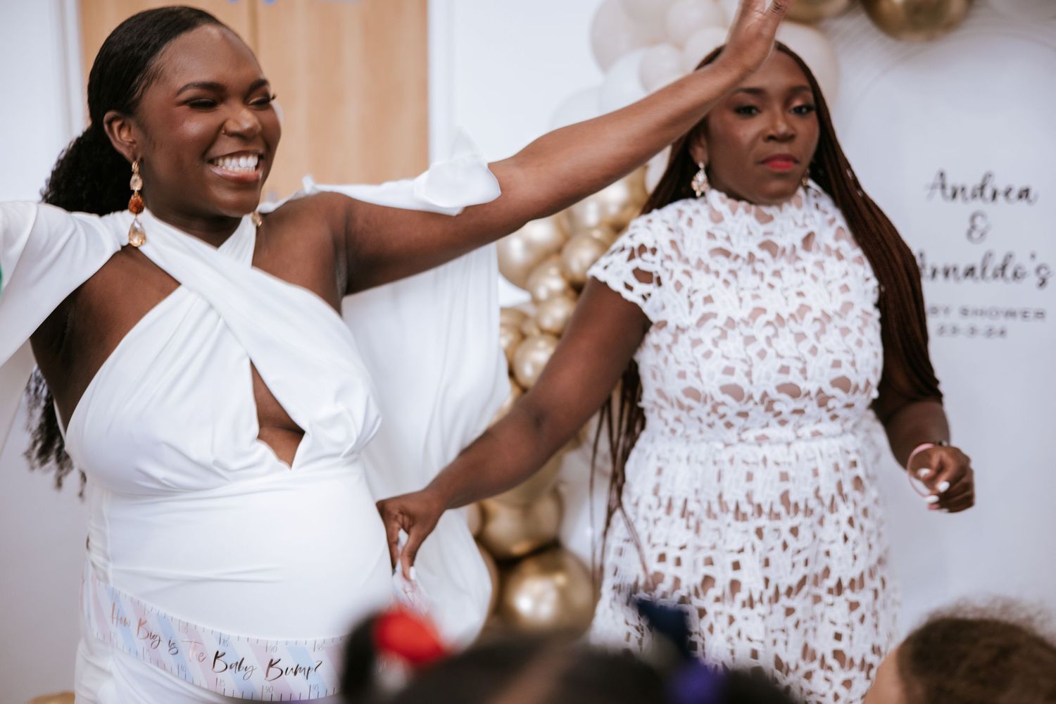 Guests enjoying a celebration in white and lace outfits against a balloon-decorated backdrop.