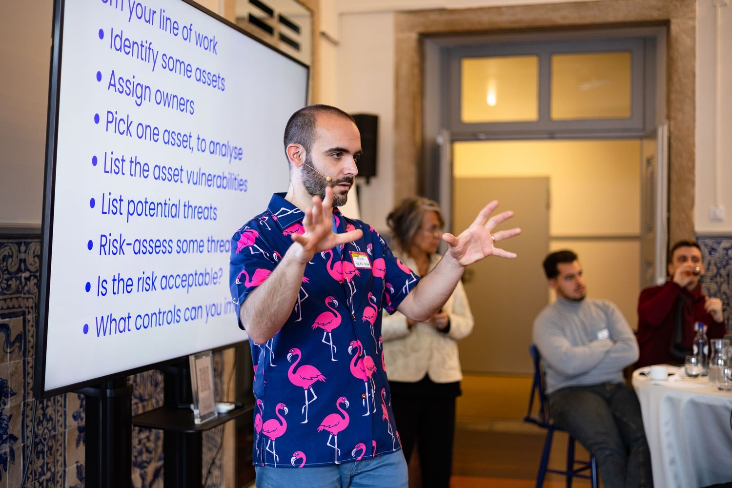 Presenter gesturing while speaking in front of a projection screen at a business event.