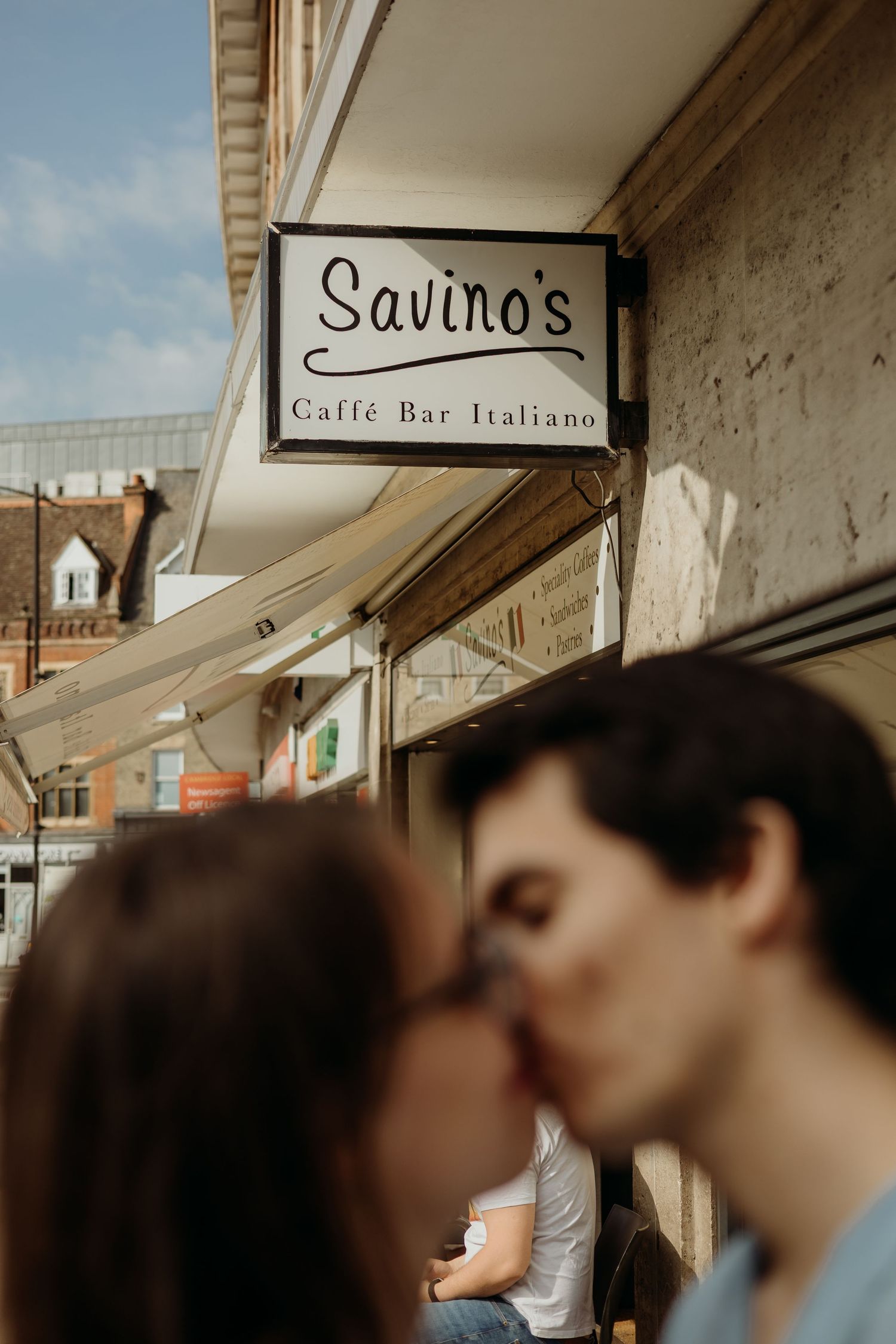 A couple shares a tender moment under a storefront sign on a city street.