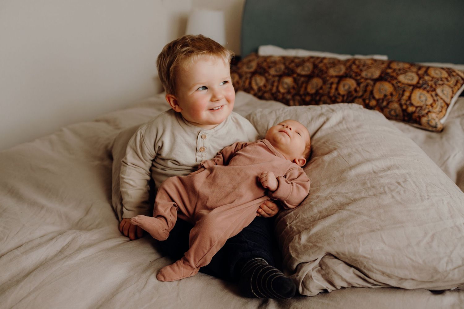 Two small children sitting together on a bed with soft lighting.