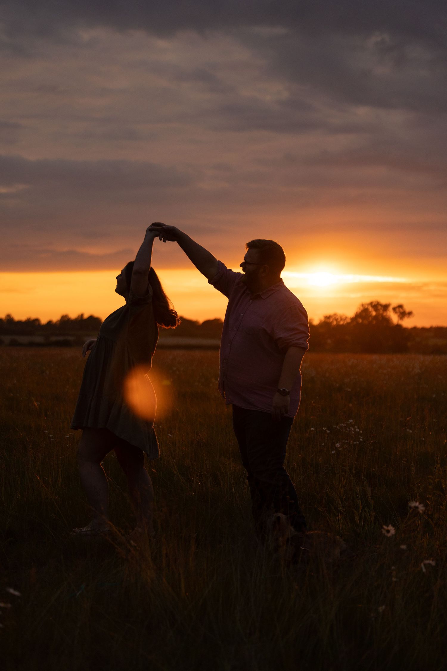 Silhouettes dancing in field against dramatic sunset sky.