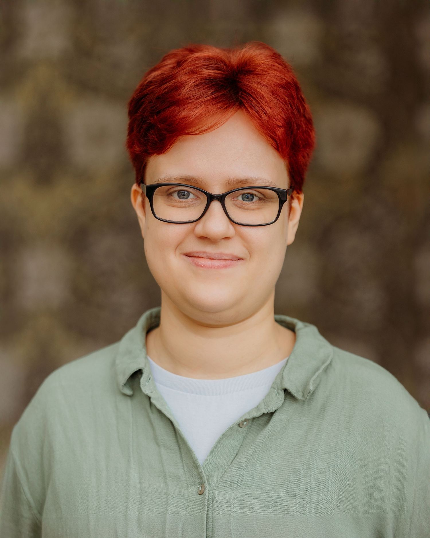 Professional headshot of person with red hair wearing glasses and sage green shirt.