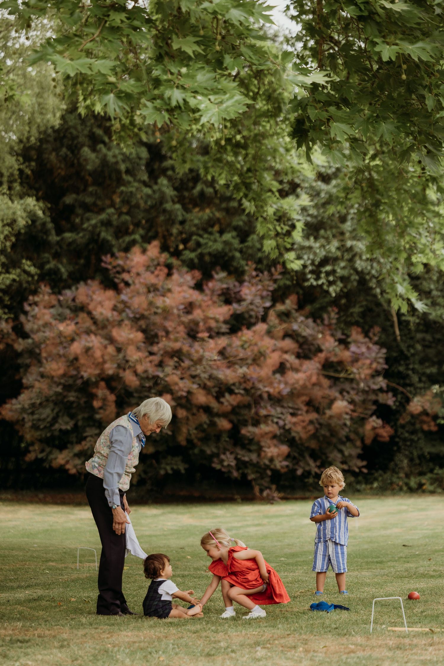 People playing croquet on a green lawn surrounded by trees and landscaping.