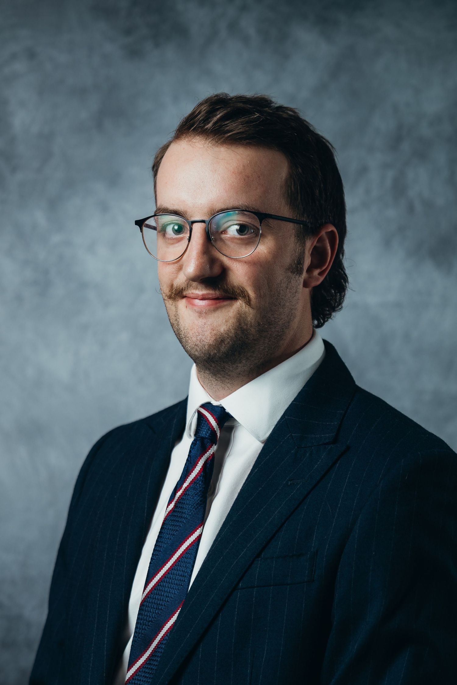 Professional studio portrait series showing different angles of someone wearing a navy suit, glasses and striped tie.