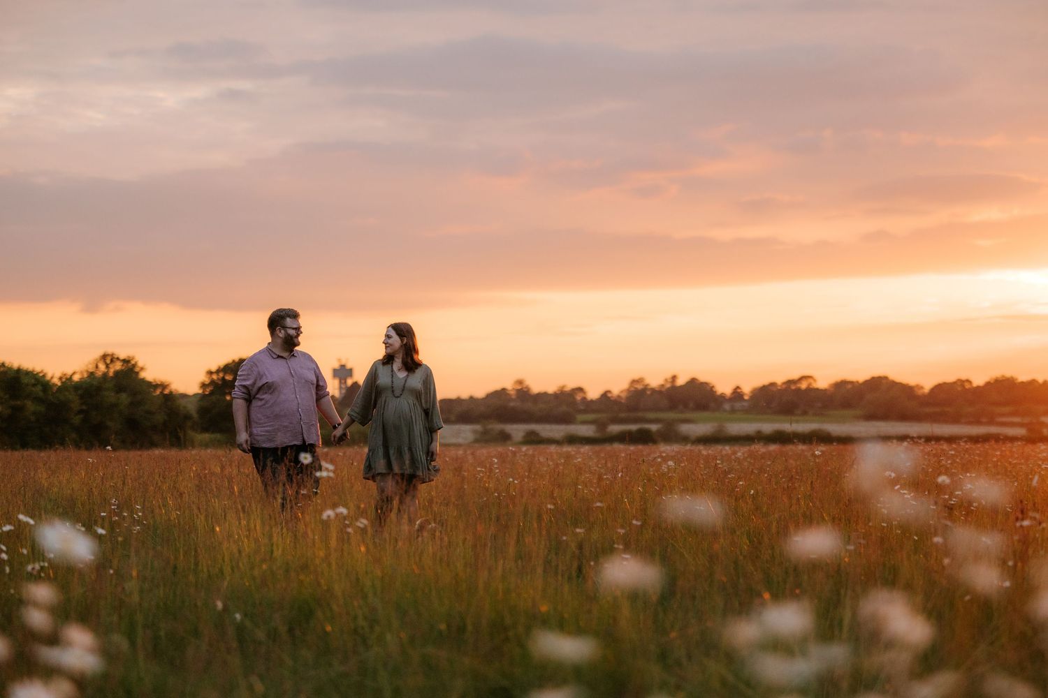 A couple walks through a golden field at sunset with dramatic lighting and long shadows.