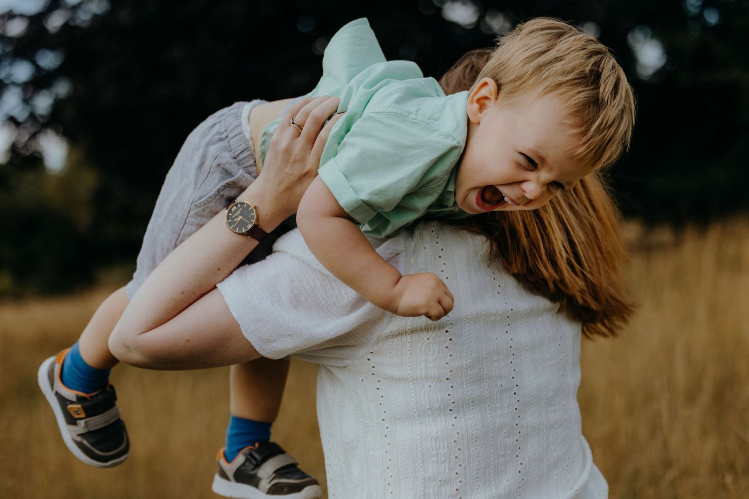 A joyful moment captured in a grassy field as a child is playfully held up in the air wearing a mint green shirt.