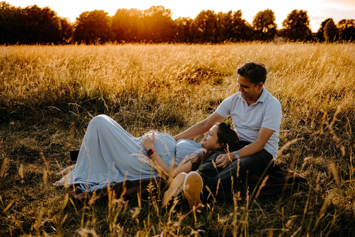 A couple sits together in a golden wheat field at sunset, creating a romantic silhouette against the warm sky.
