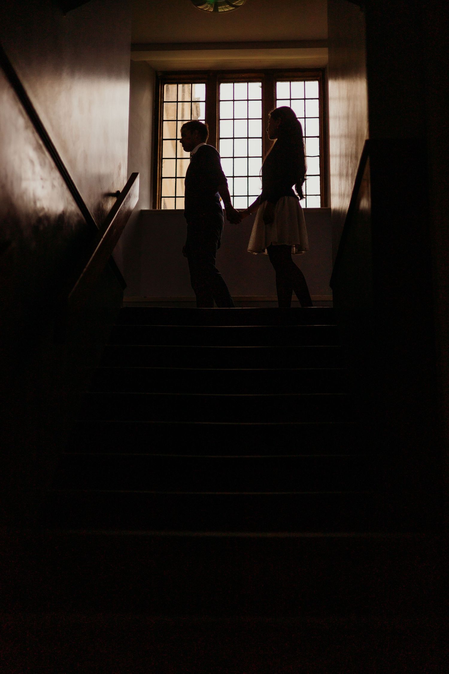 Silhouettes of people walking through a dimly lit historic interior hallway.