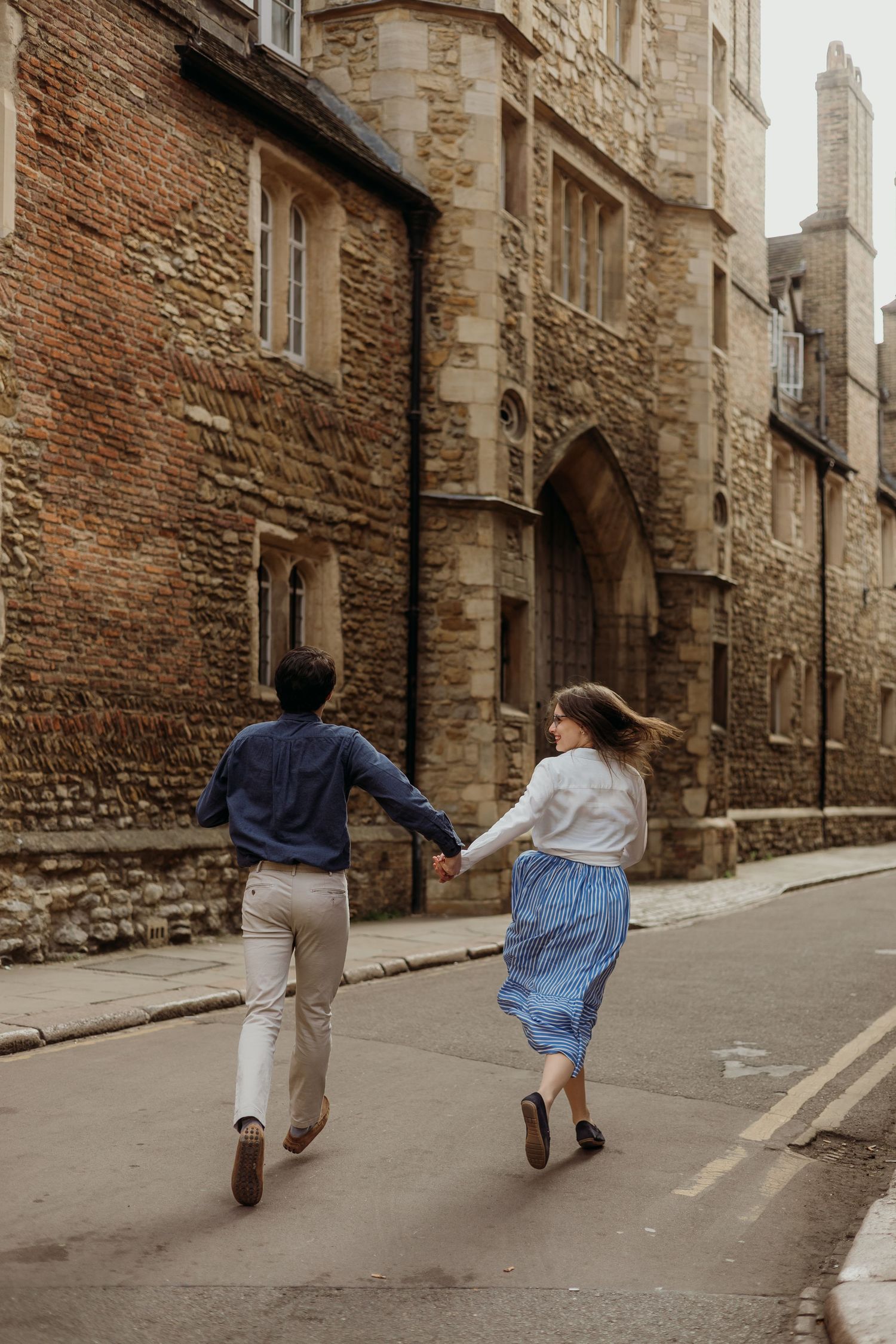Two people run playfully down an old brick-lined street in a historic district.