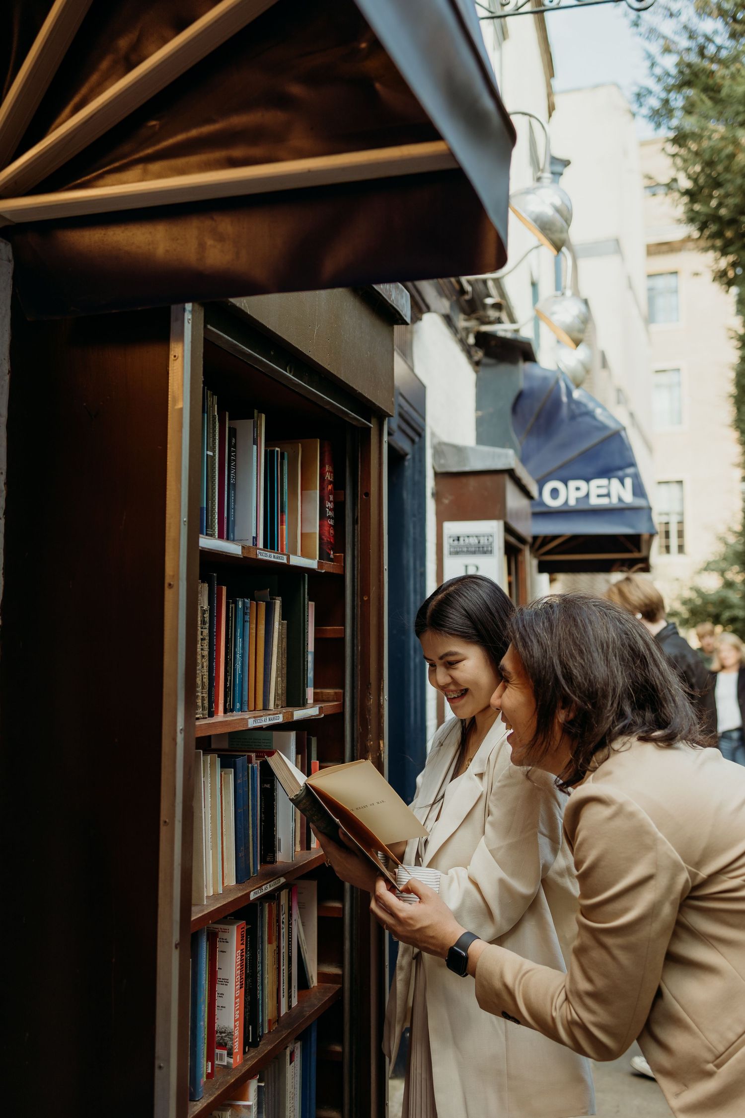 Person in beige coat browsing books on wooden library shelves.