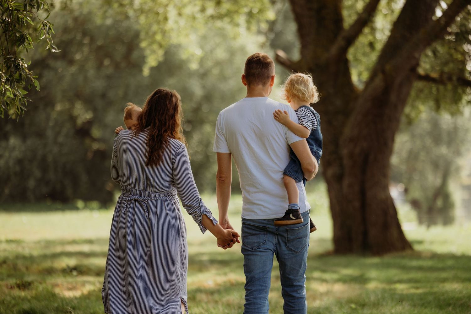 Family walking together through sunlit park holding hands.