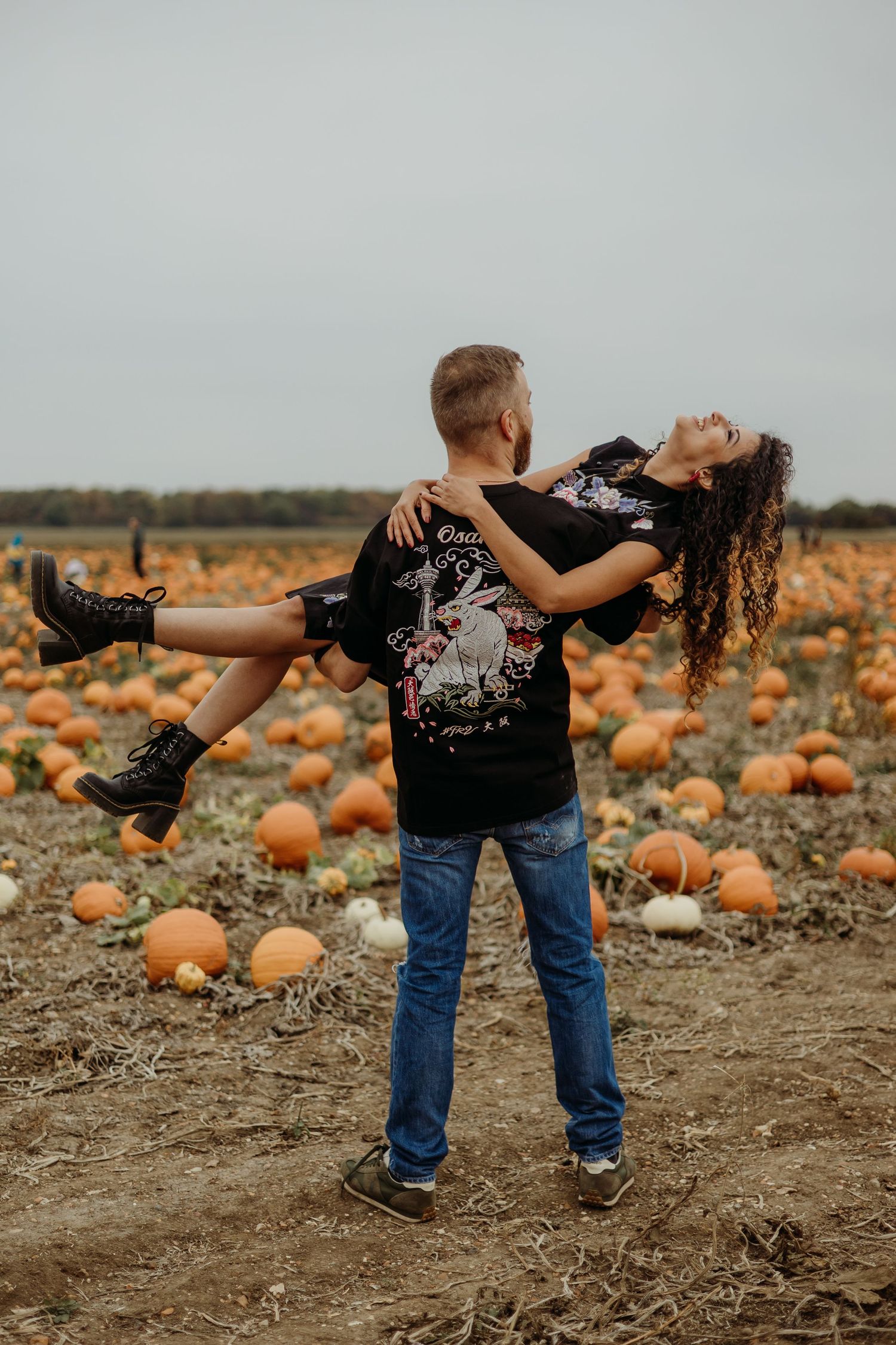 Playful couple dances together in a pumpkin patch field at sunset.