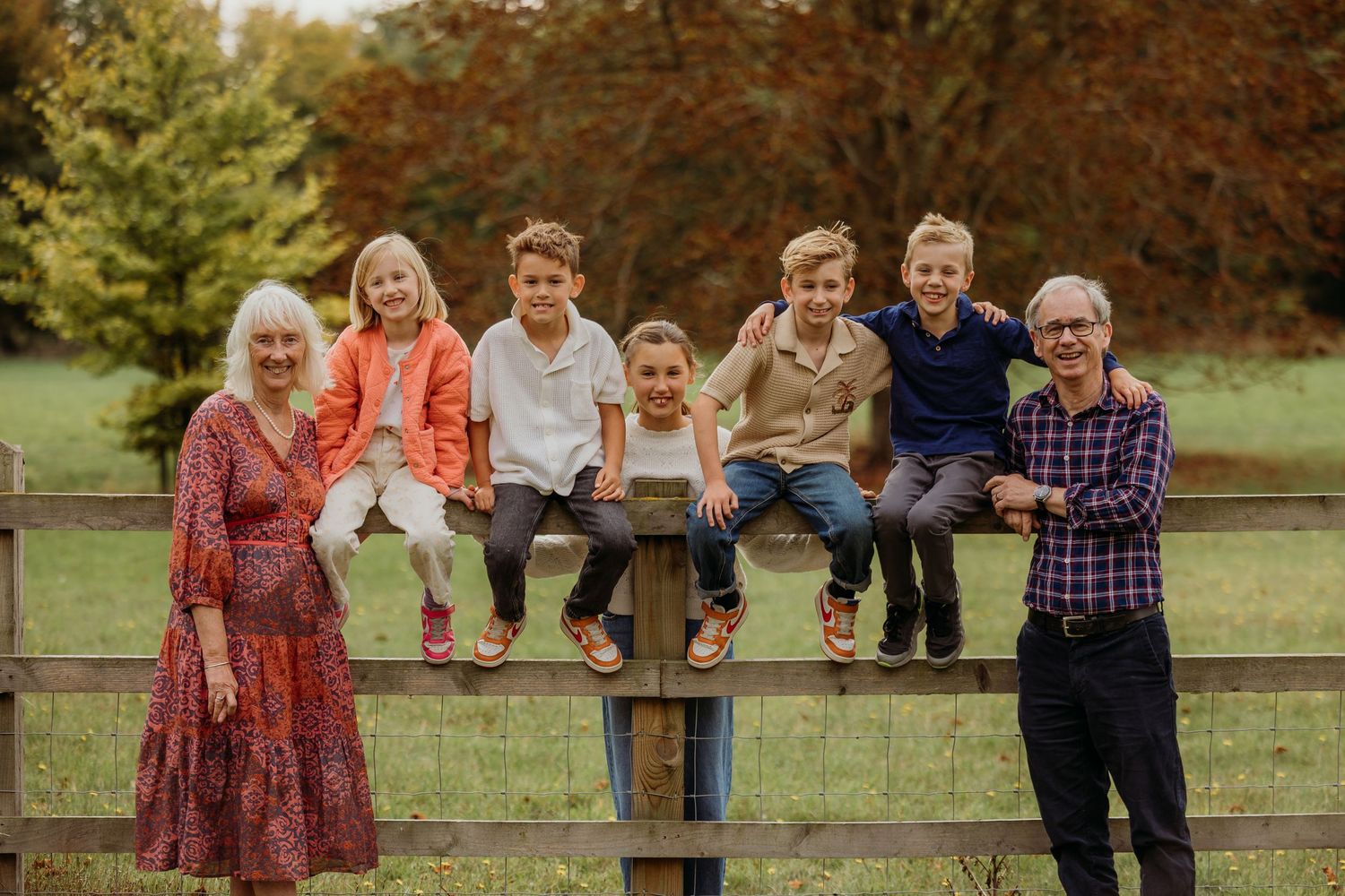 Family group sitting together on a wooden fence during autumn.