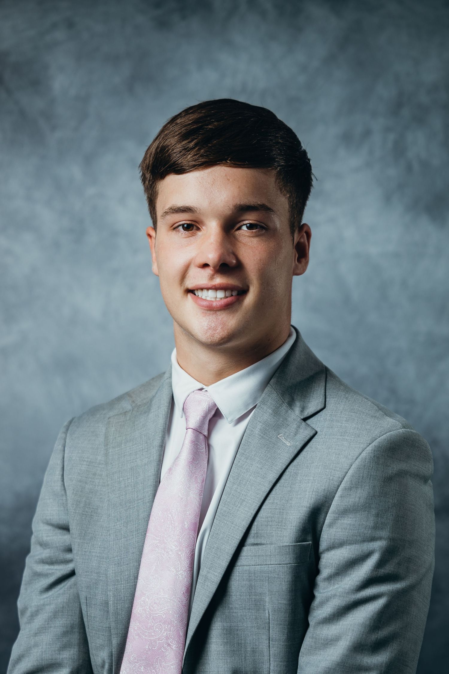 Professional headshot series showing a person in a gray suit and pink tie against a textured gray background.