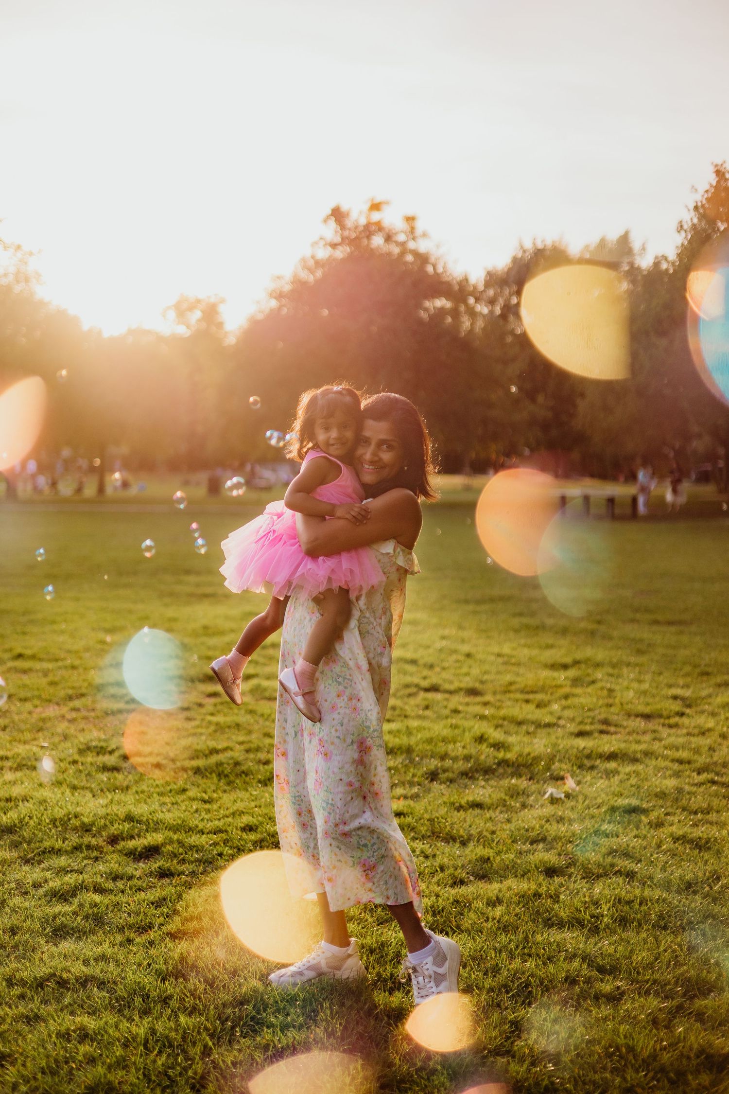 Young child in pink dress playing in a grassy field during golden hour.