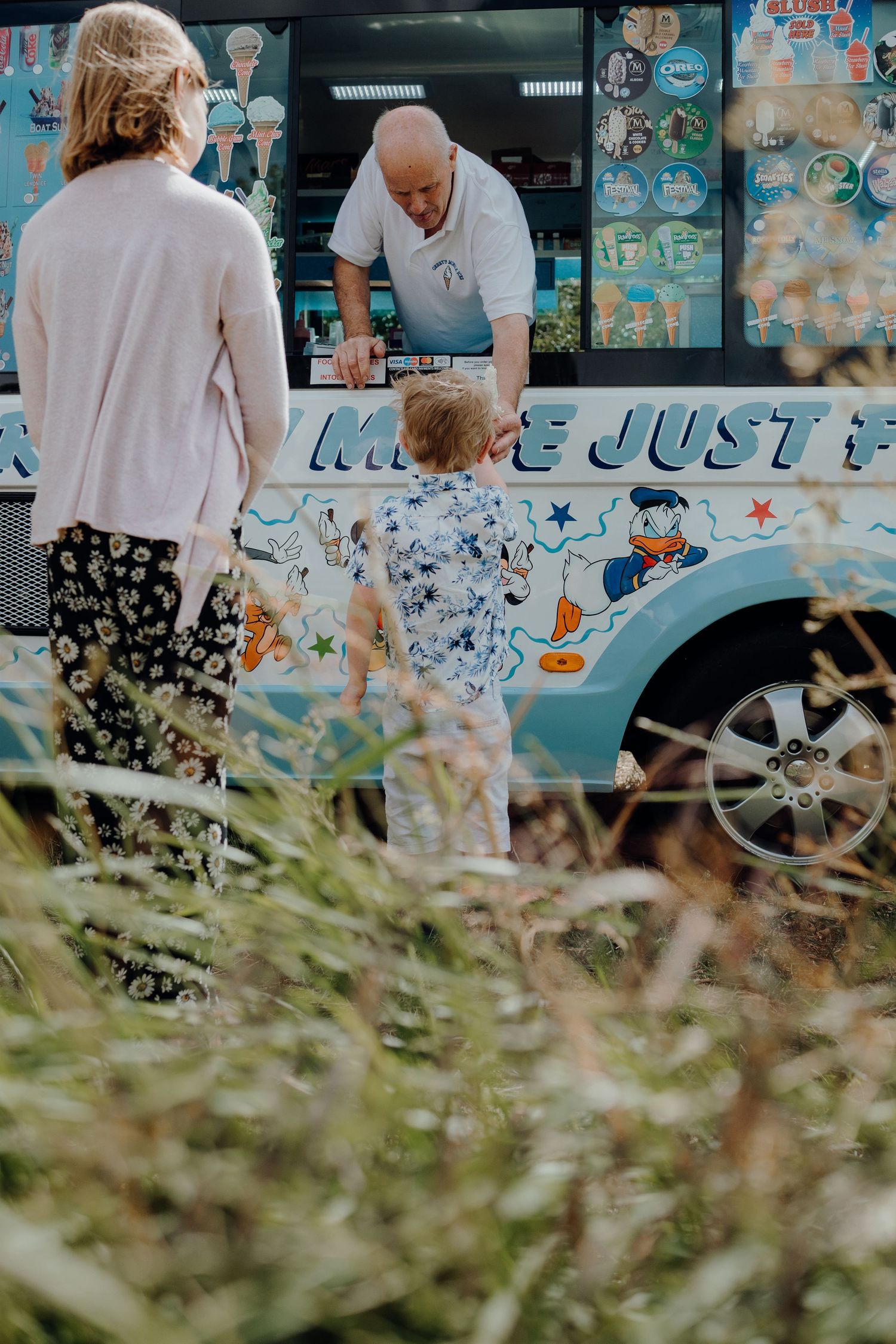 Ice cream truck with decorative graphics parked at outdoor event with grass in foreground.
