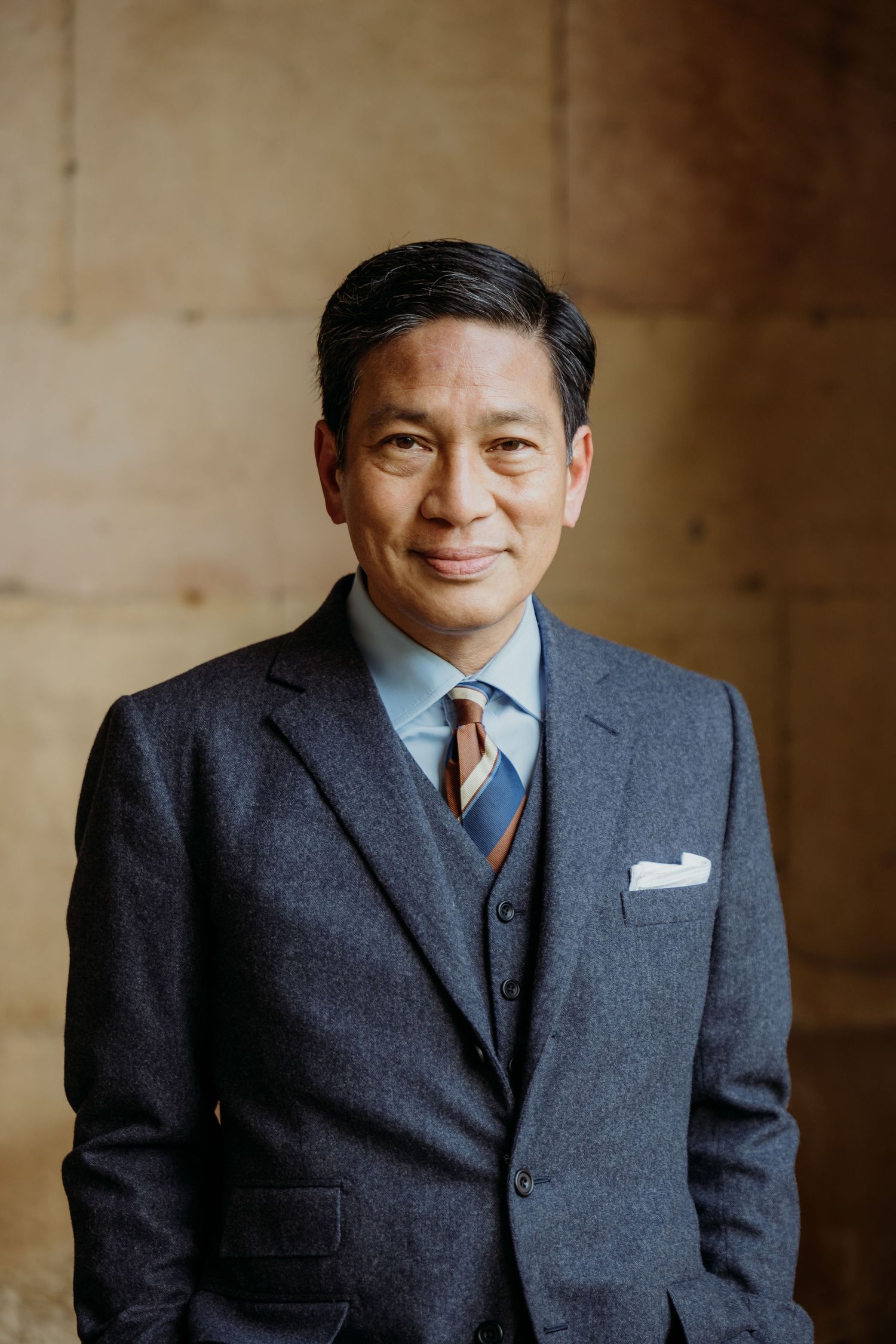 Professional portraits of someone in a dark business suit against a warm-toned background.