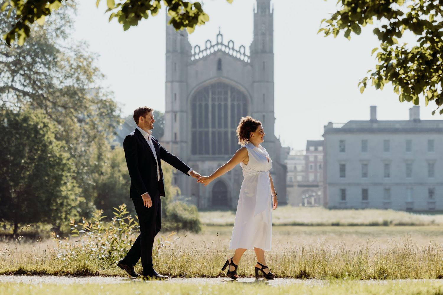 Couple walking on grass with gothic cathedral architecture in background.
