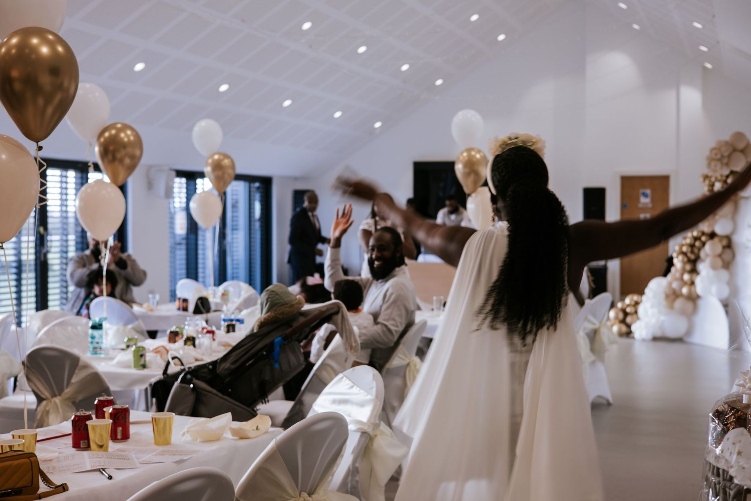 Wedding reception venue decorated with gold balloons and white tables set for celebration.