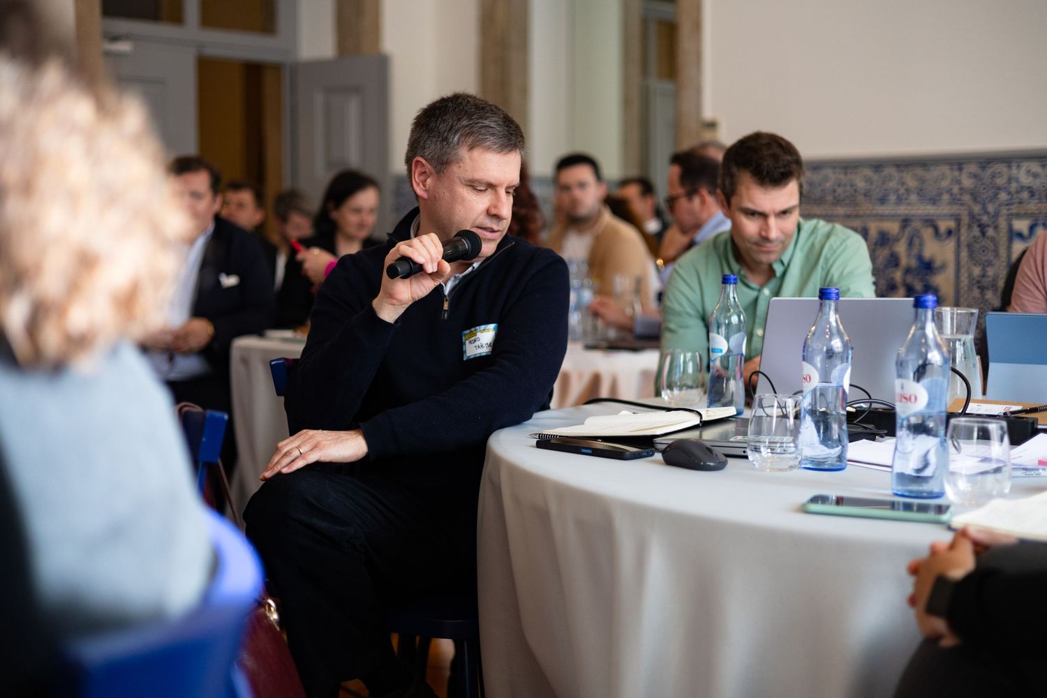 People seated at round tables during a professional conference or workshop.