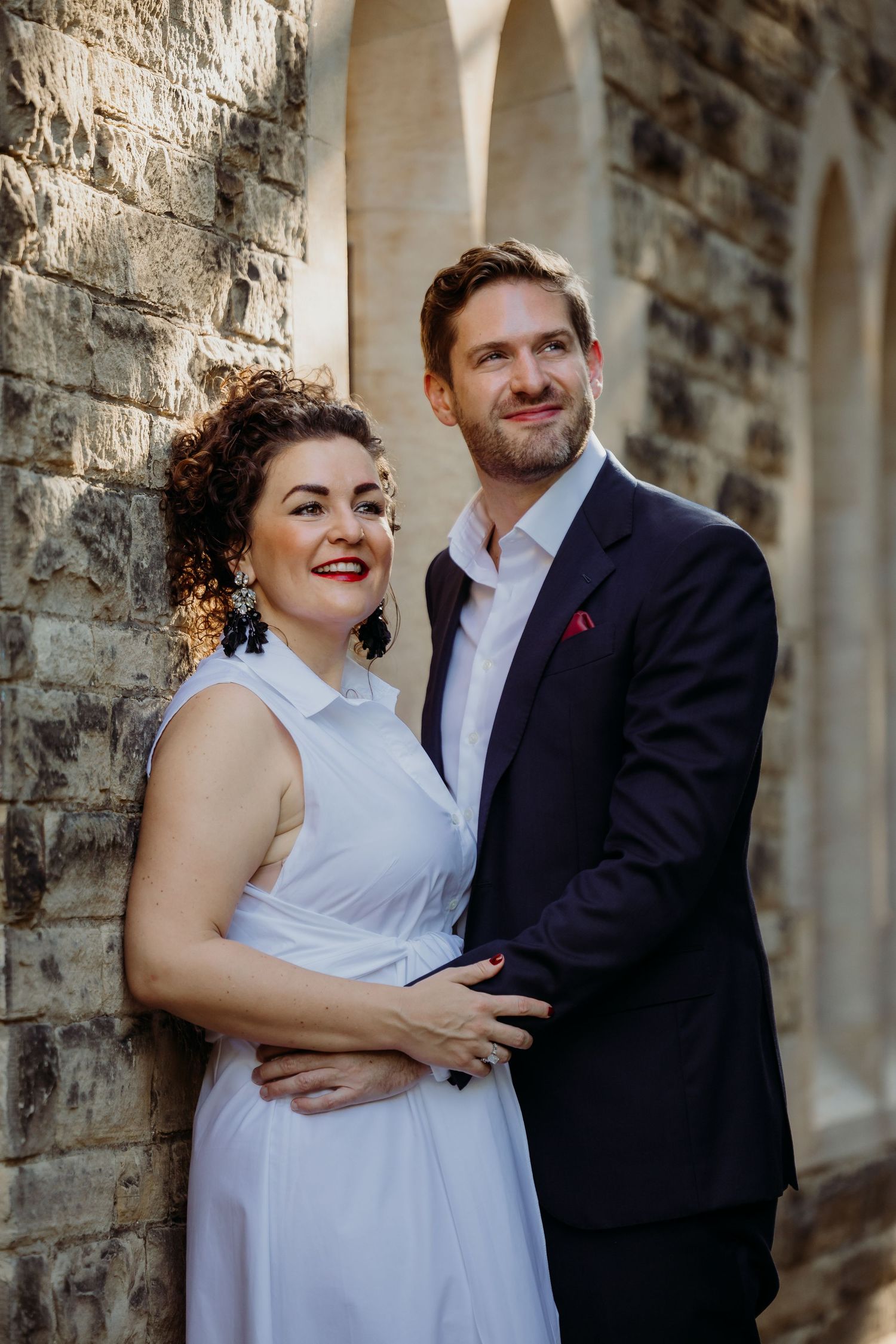 Couple in formal attire sharing a candid moment against stone wall.