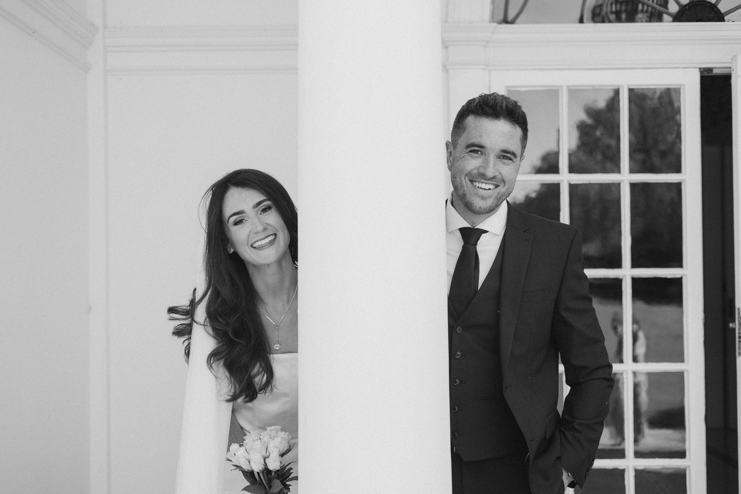 Wedding couple poses in an elegant white interior with classic architectural details.