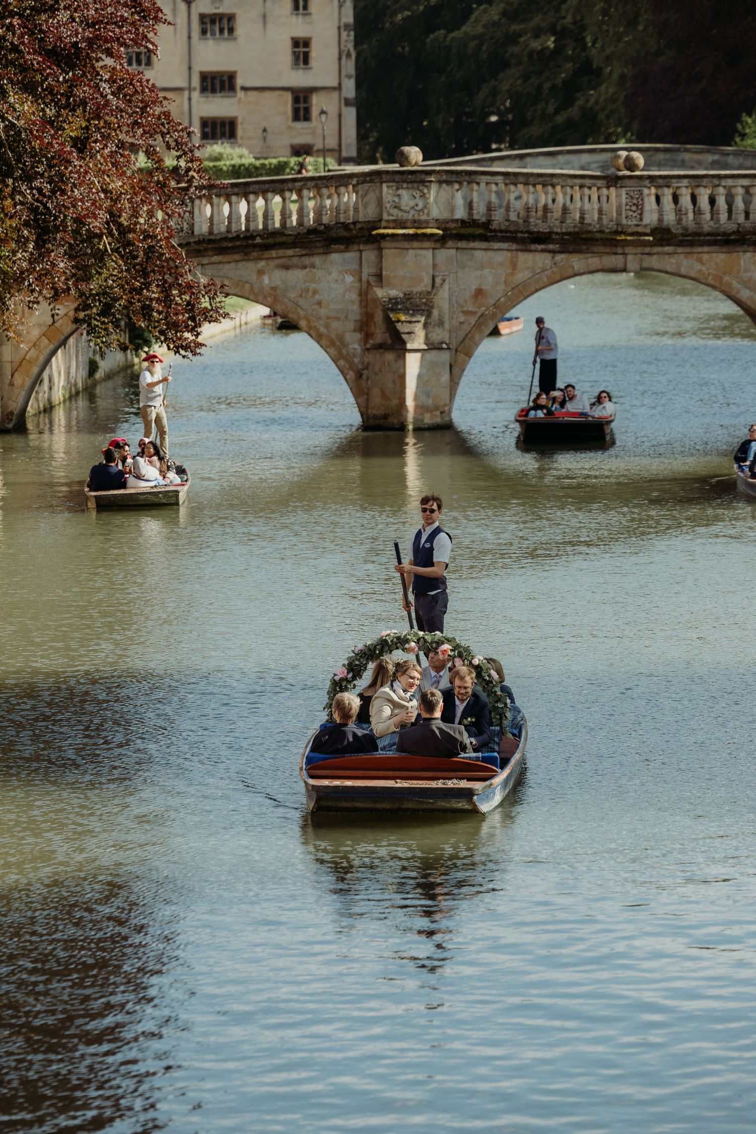 Multiple punting boats navigate through historic waterways under stone bridges.