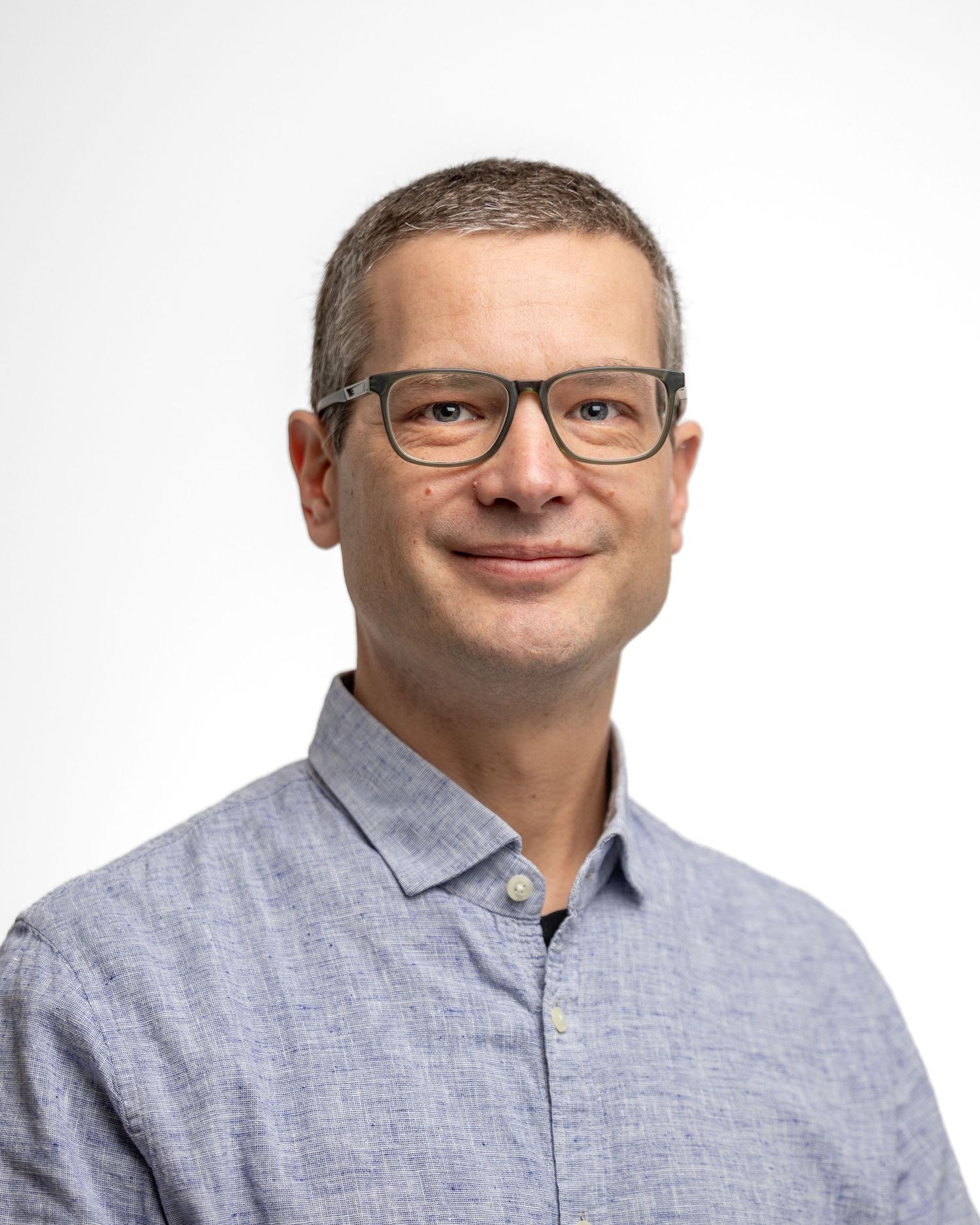 Professional headshot of someone wearing glasses and grey button-down shirt.