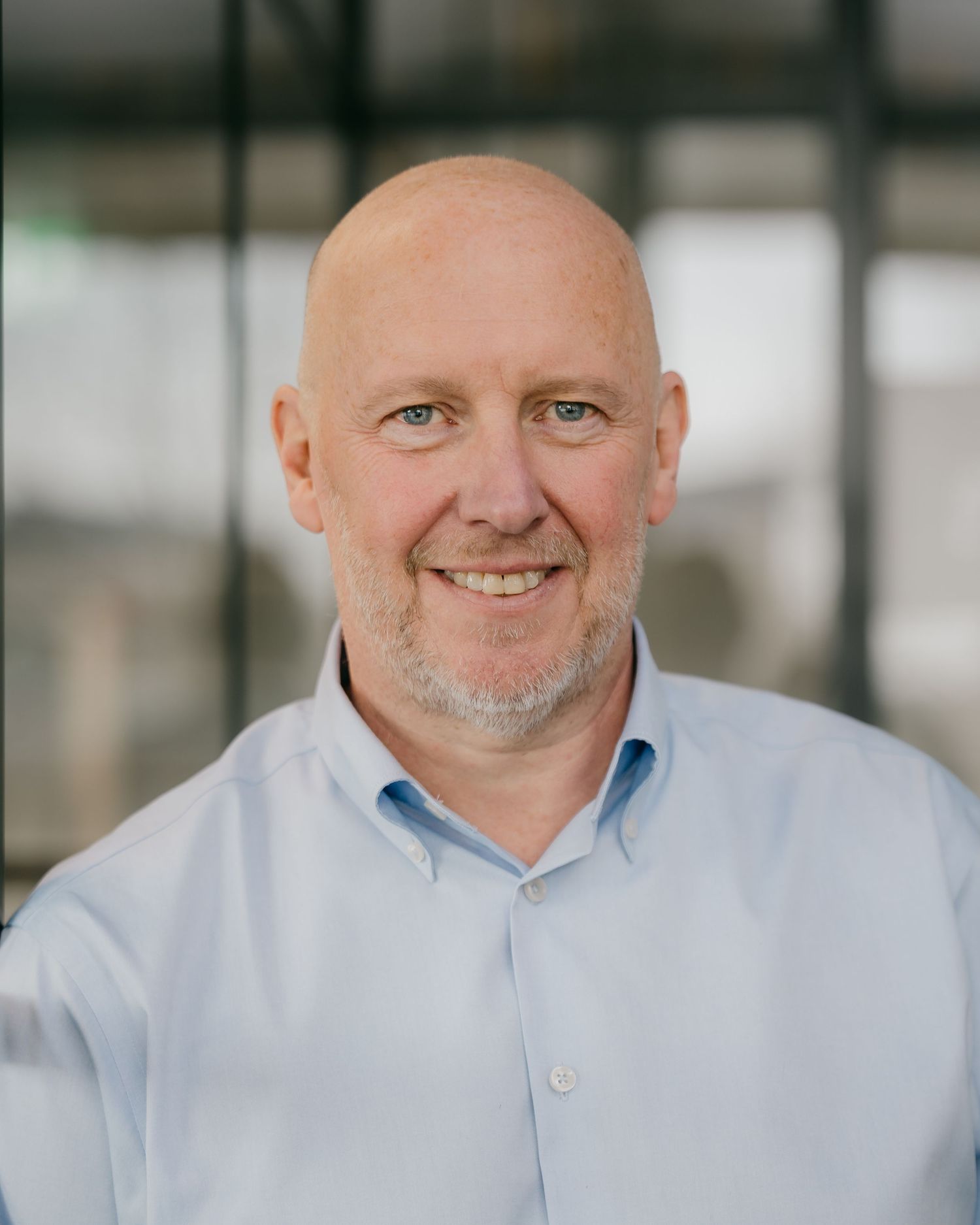 Professional headshot of a bald man in a light blue button-down shirt smiling at the camera.