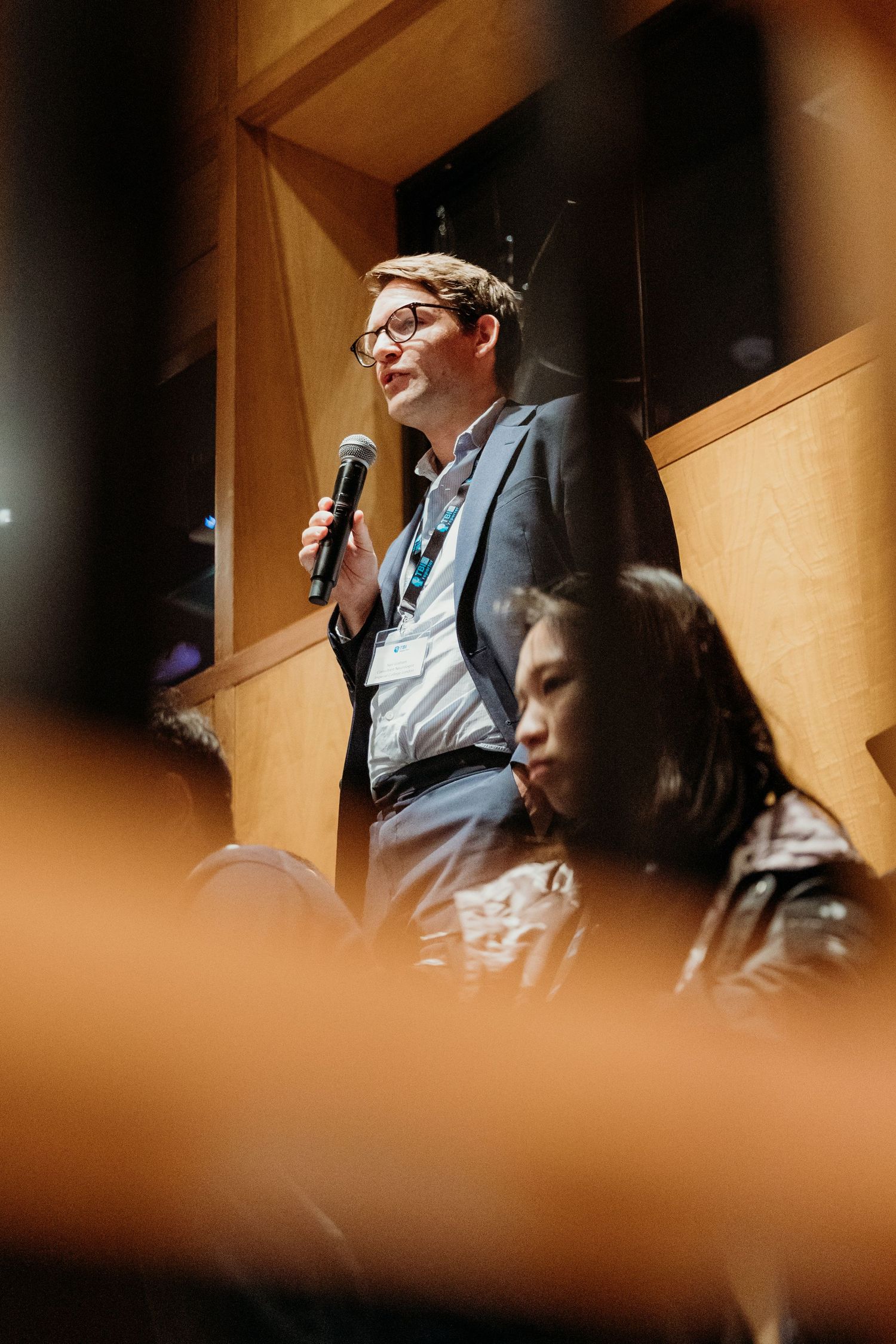 A speaker addresses an audience from a podium in a dimly lit auditorium.