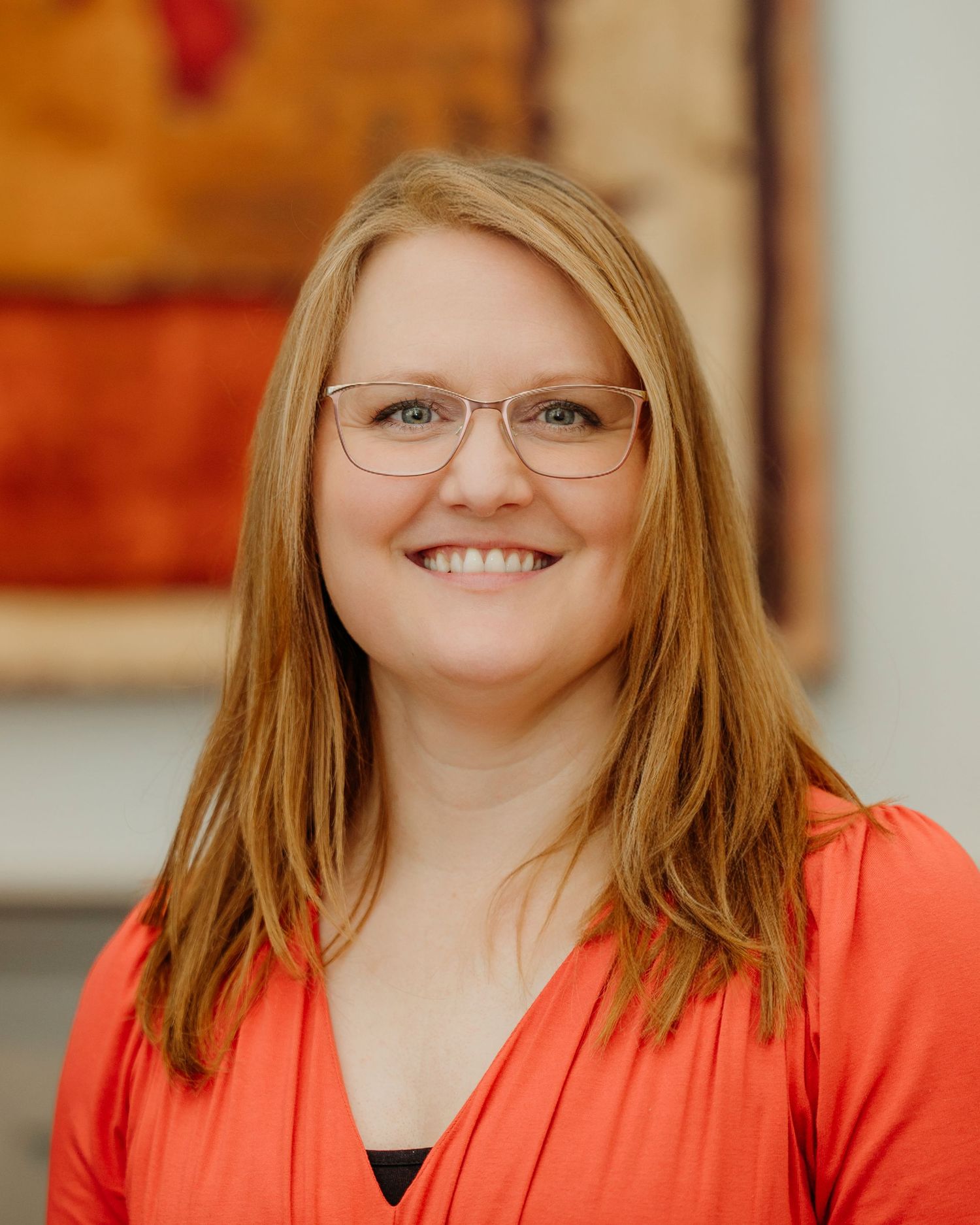 Professional headshot of someone in a coral blazer and glasses against a light background.