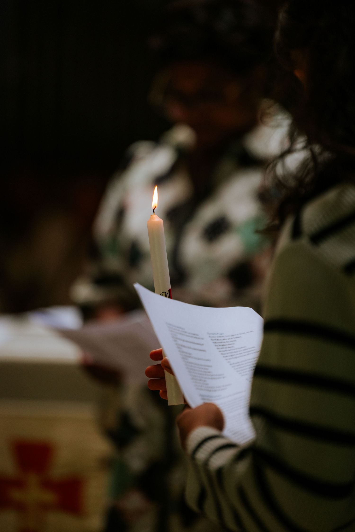Hands holding papers and candles during a dimly lit ceremony.