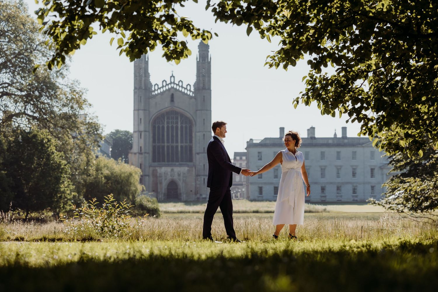 A couple holds hands in front of a grand cathedral building during golden hour.