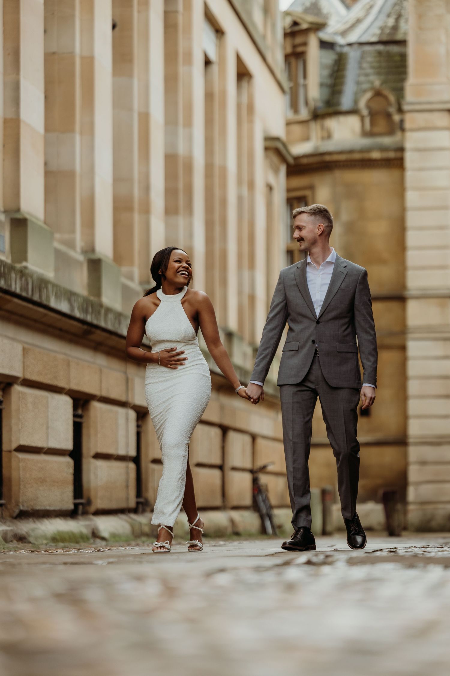 A couple in wedding attire walks together along a grand architectural colonnade.