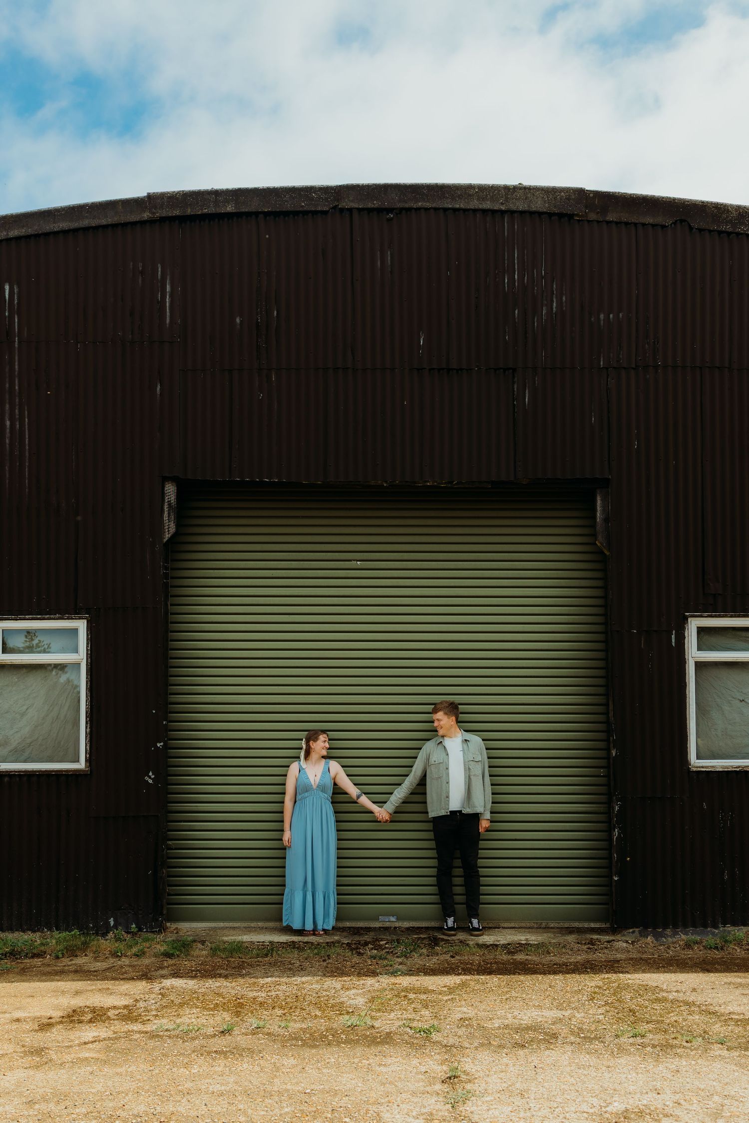 Couple posing against industrial green metal doors of warehouse building.