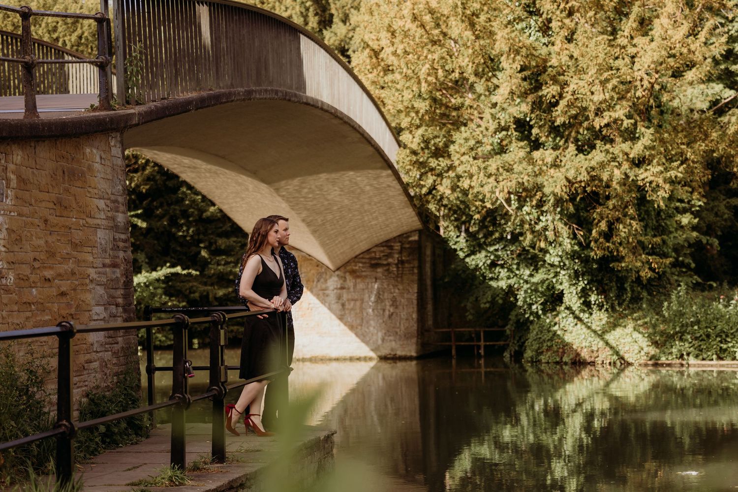 Stone bridge reflection over calm water with overhanging trees creating natural frame.