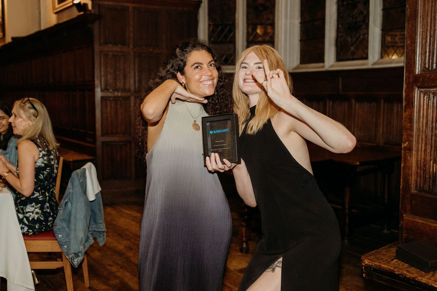 People dancing and socializing at an evening event in a wood-paneled hall.