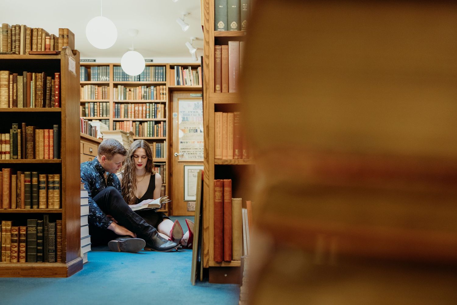 A cozy reading moment between people in a library surrounded by wooden bookshelves.