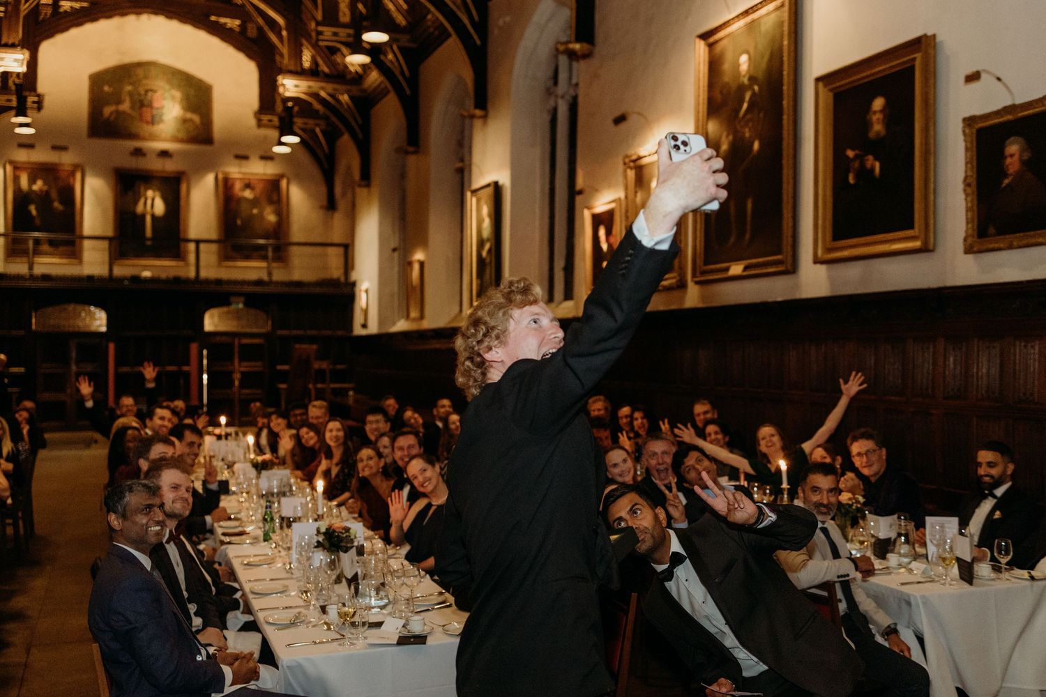 Formal dinner setup in historic hall with portrait-lined walls and elegant table settings.