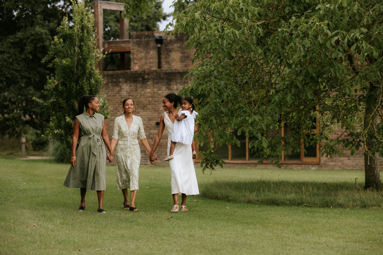 People walking together on a lush green lawn near historic brick buildings.