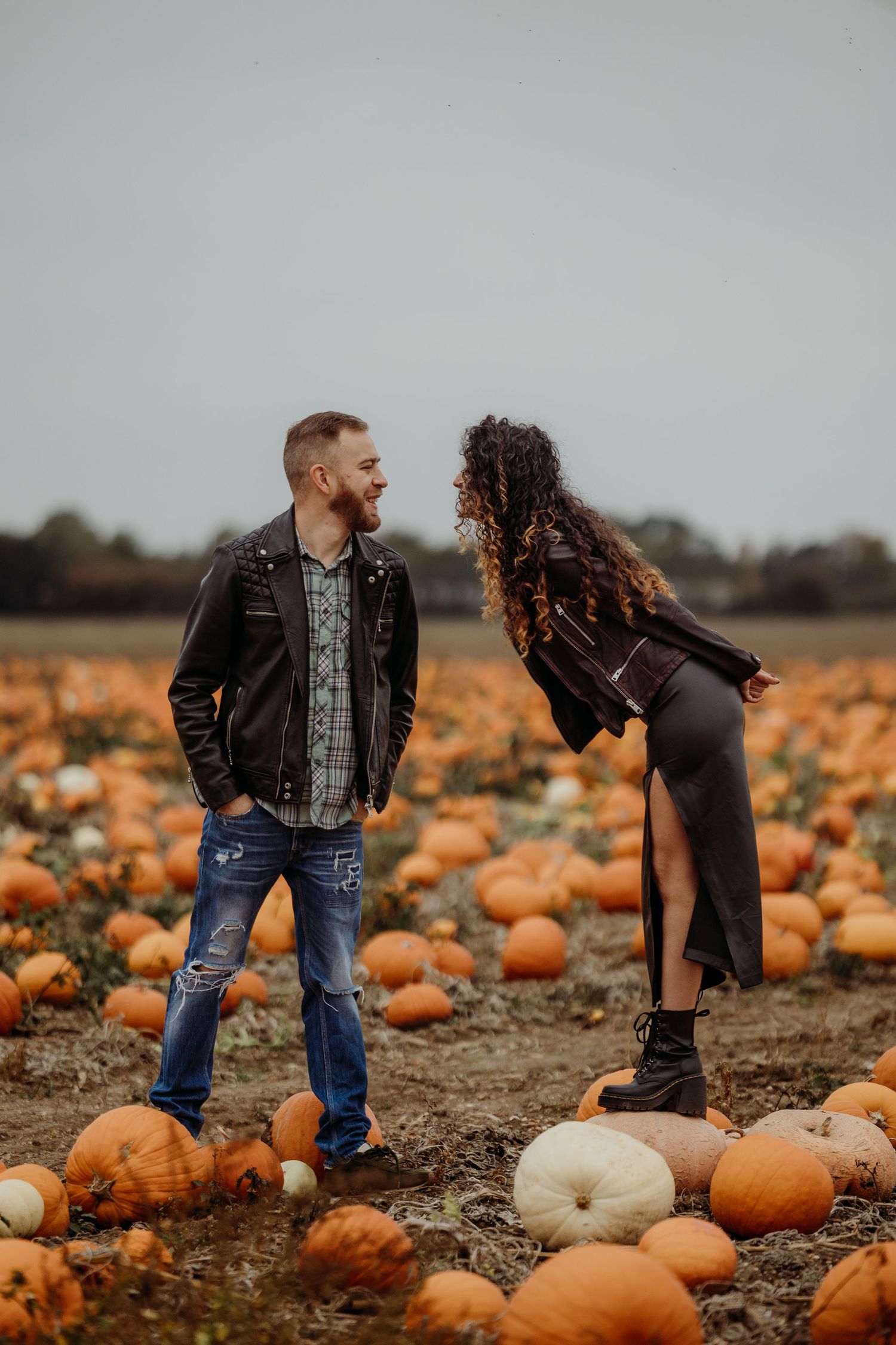 Romantic couple poses and dances among orange pumpkins in a harvest field.