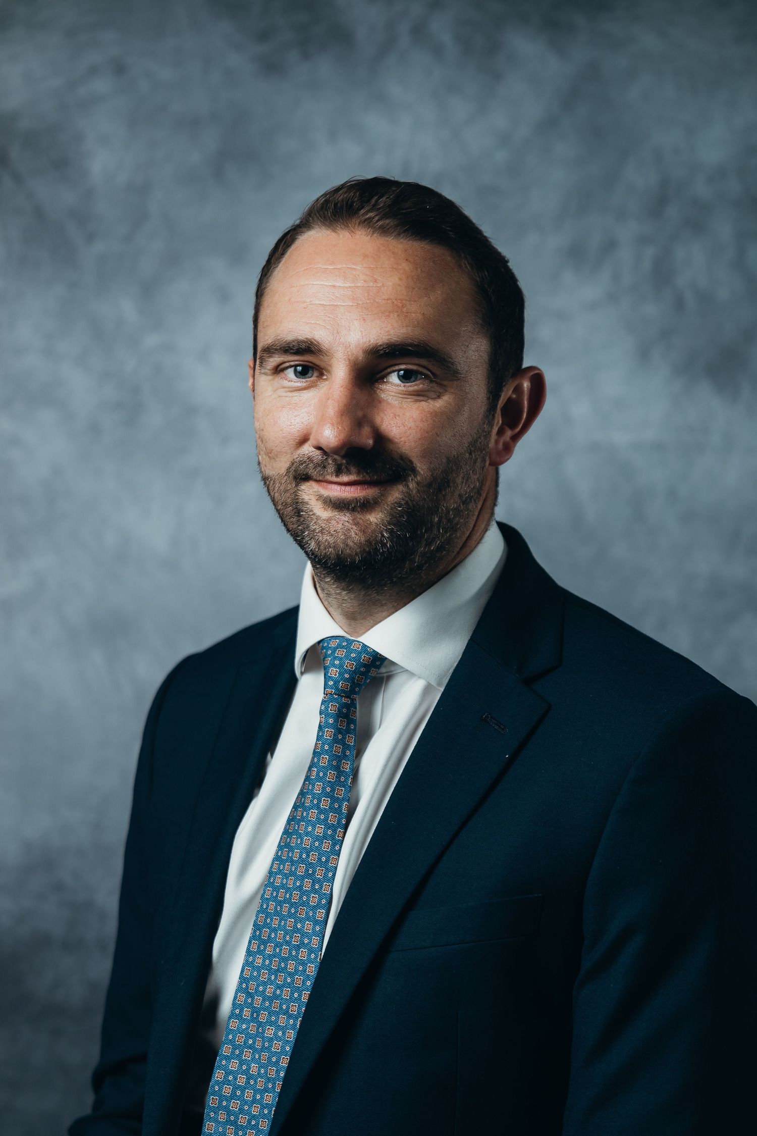 Professional portrait series featuring a person in a navy suit and patterned blue tie against a gray backdrop.