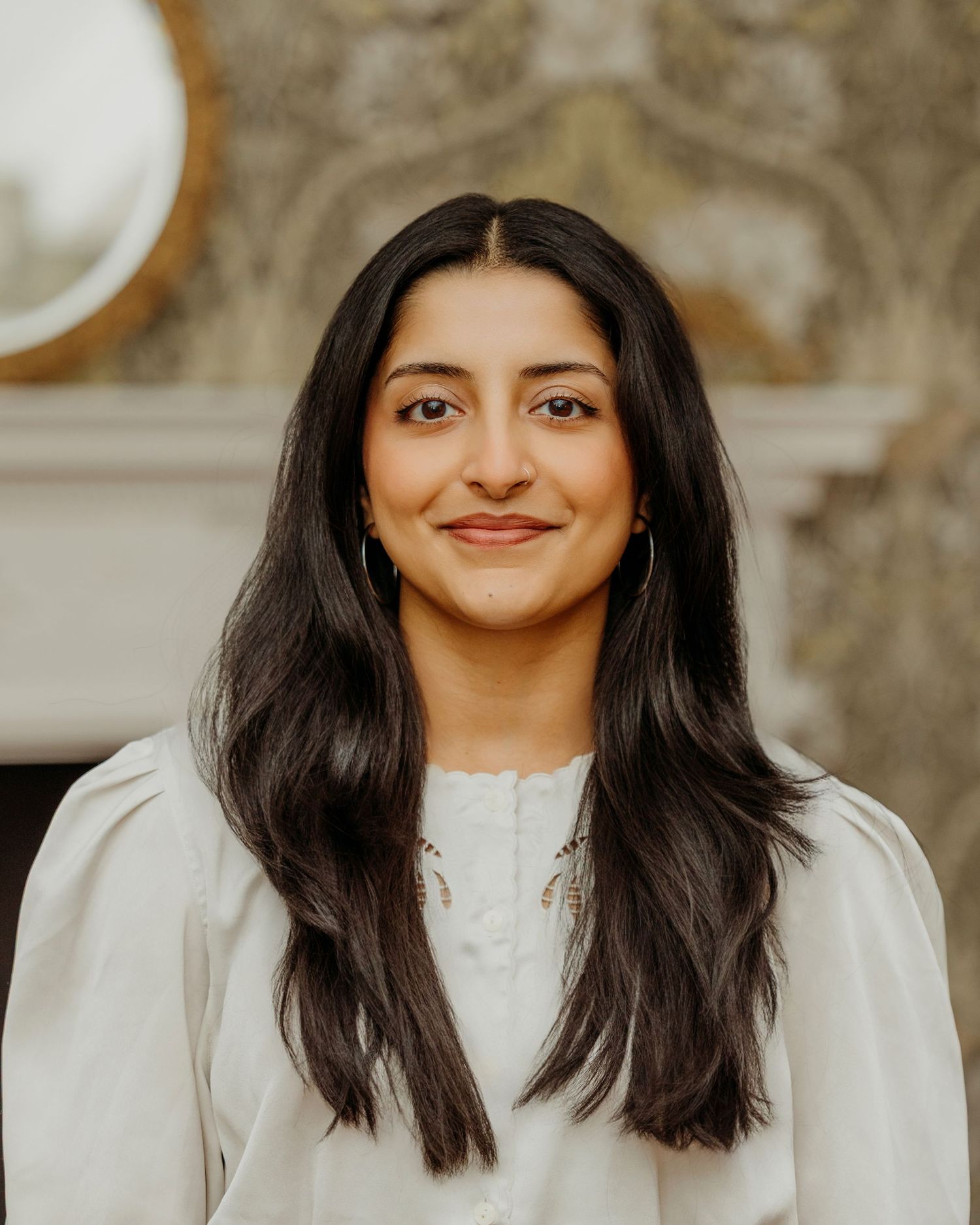 Portrait of person with long dark hair wearing white top against neutral background.