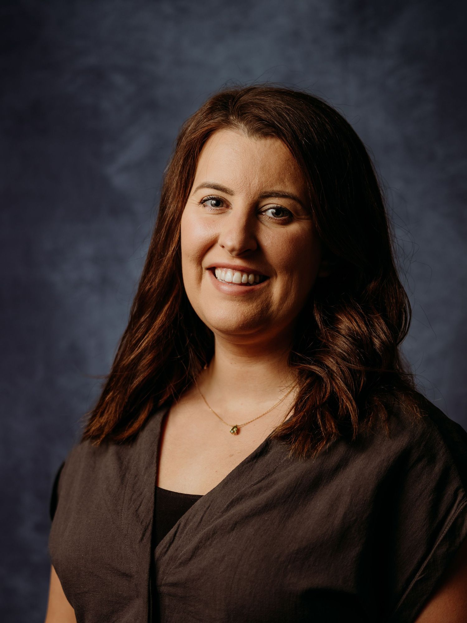 Studio portrait of someone in dark clothing against a moody background.