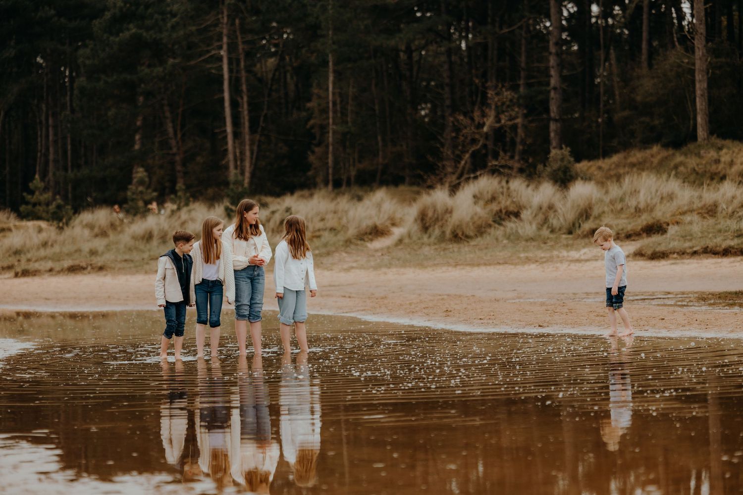 Family wearing coordinated blue and white outfits walks along a scenic beach at sunset.