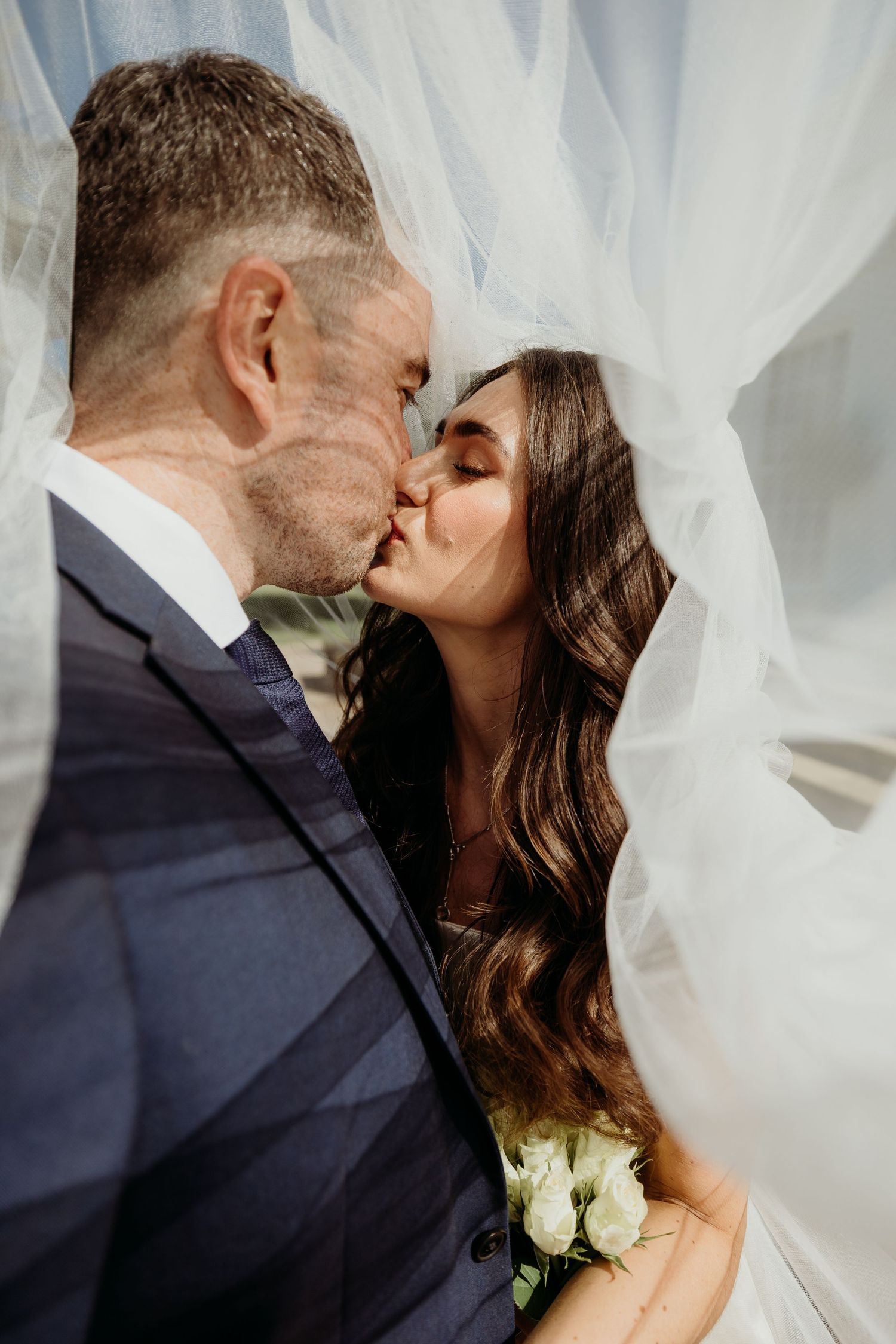 A romantic wedding kiss sequence with flowing white veil and dark suit against a light background.