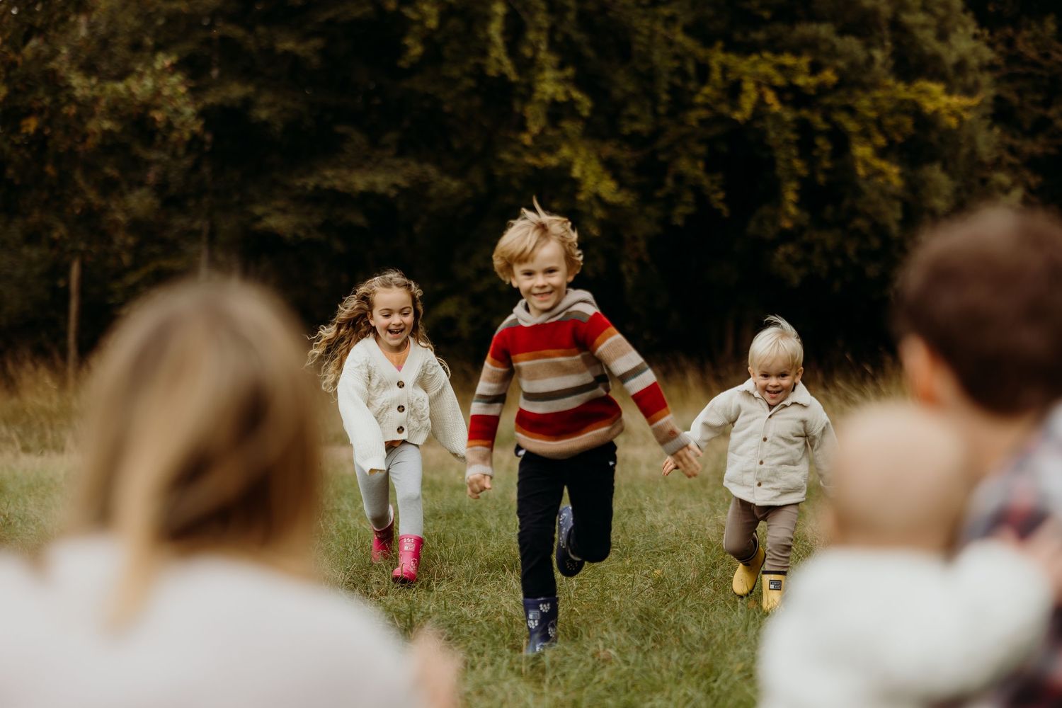 A group of people running and playing together in a grassy field on a sunny autumn day.