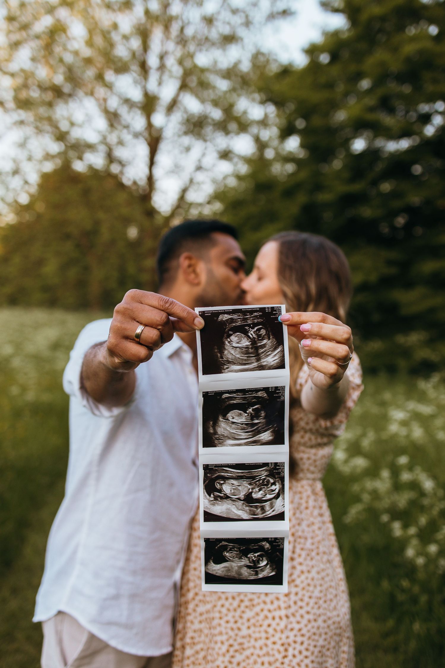 A couple outdoors holds up an ultrasound photo in a series of joyful pregnancy announcement photos.