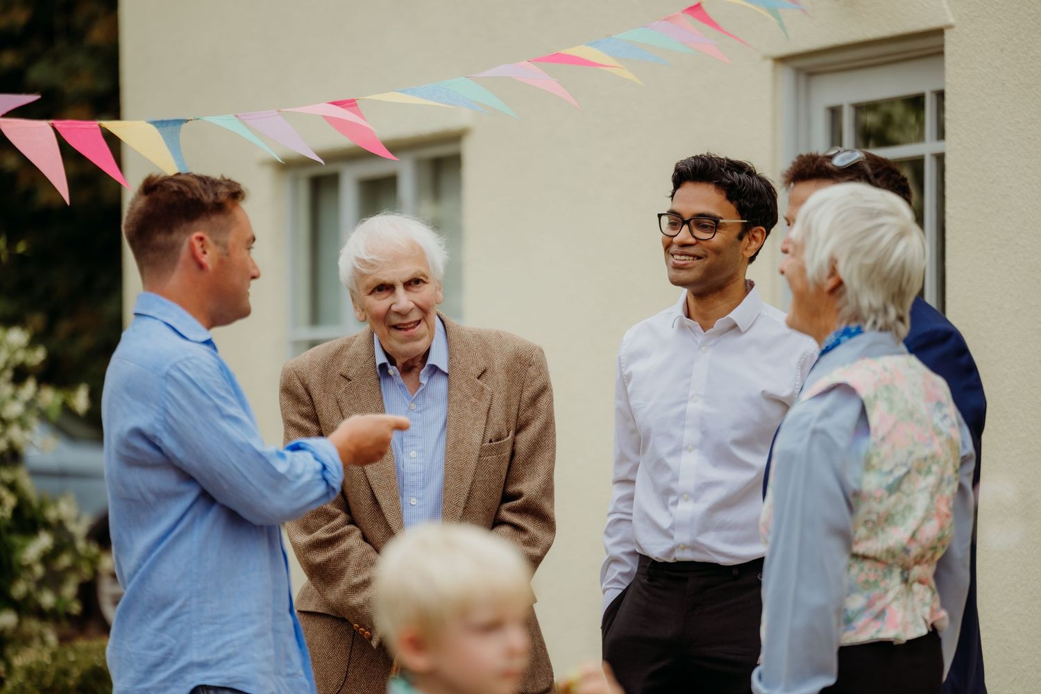 People gathered outdoors for a celebration with colorful triangle bunting decorations hanging overhead.